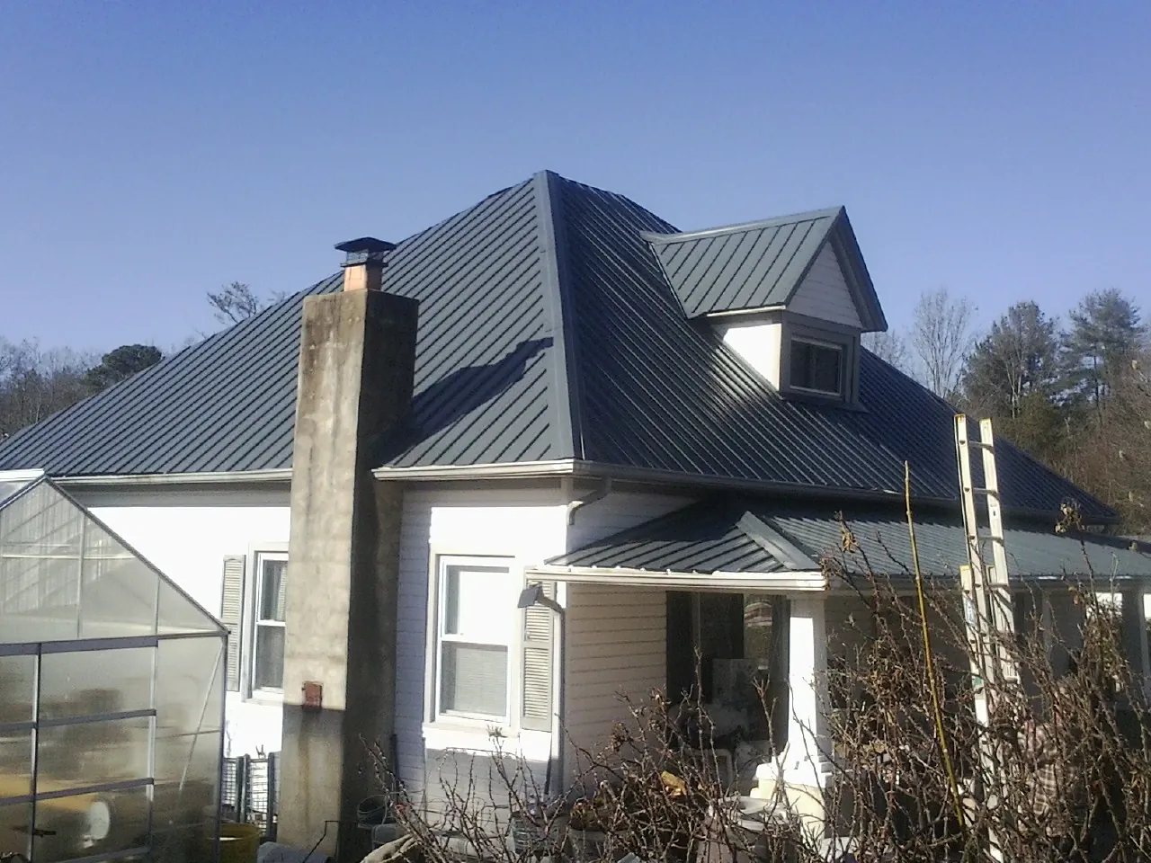 Dark blue standing seam metal roof on a white farmhouse with dormer — Slate & Tile Roof Repair by Roofing Brothers in New Bern