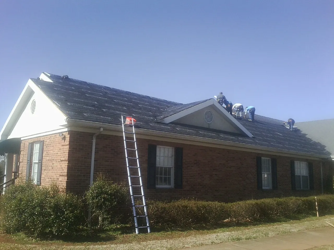 Crew tearing shingles off a brick ranch roof with a ladder set — Metal Roof Repair work by our crew in New Bern