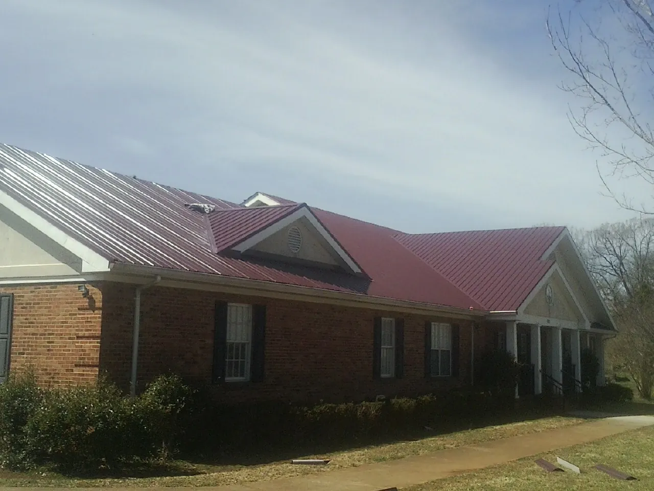 Red metal roof with gabled entries on a long brick building, from a Hail Damage Roof Repair job in New Bern