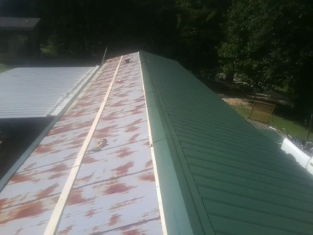 Old rusted panels beside newly installed green metal roofing in New Bern