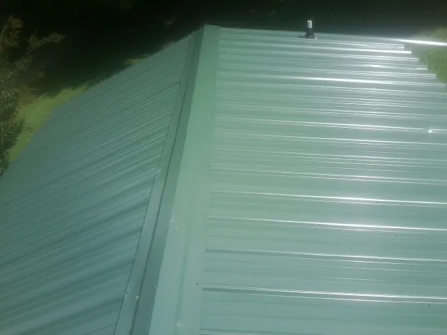 New green metal panels meeting at the ridge of a roof — Flat Roof Repair work by our crew in New Bern