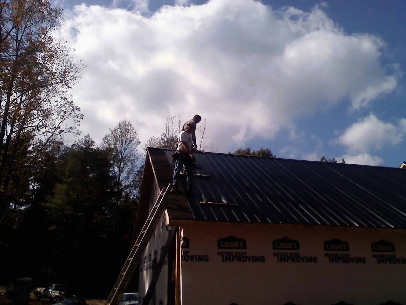 Roofer fastening dark metal panels high against a cloudy sky, from a Roof Inspection job in New Bern